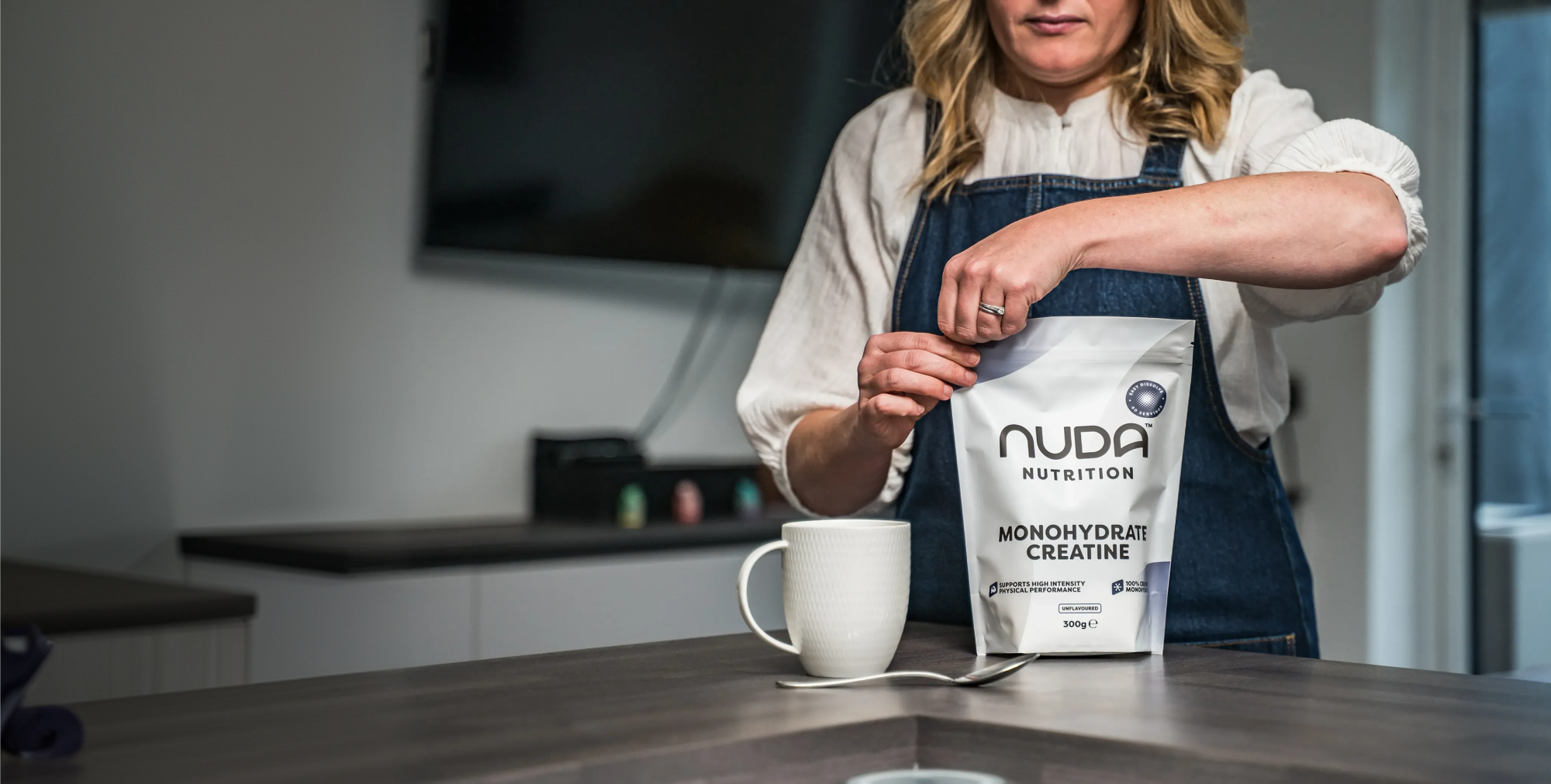 Person holding a Nuda Nutrition protein powder bag in a kitchen setting