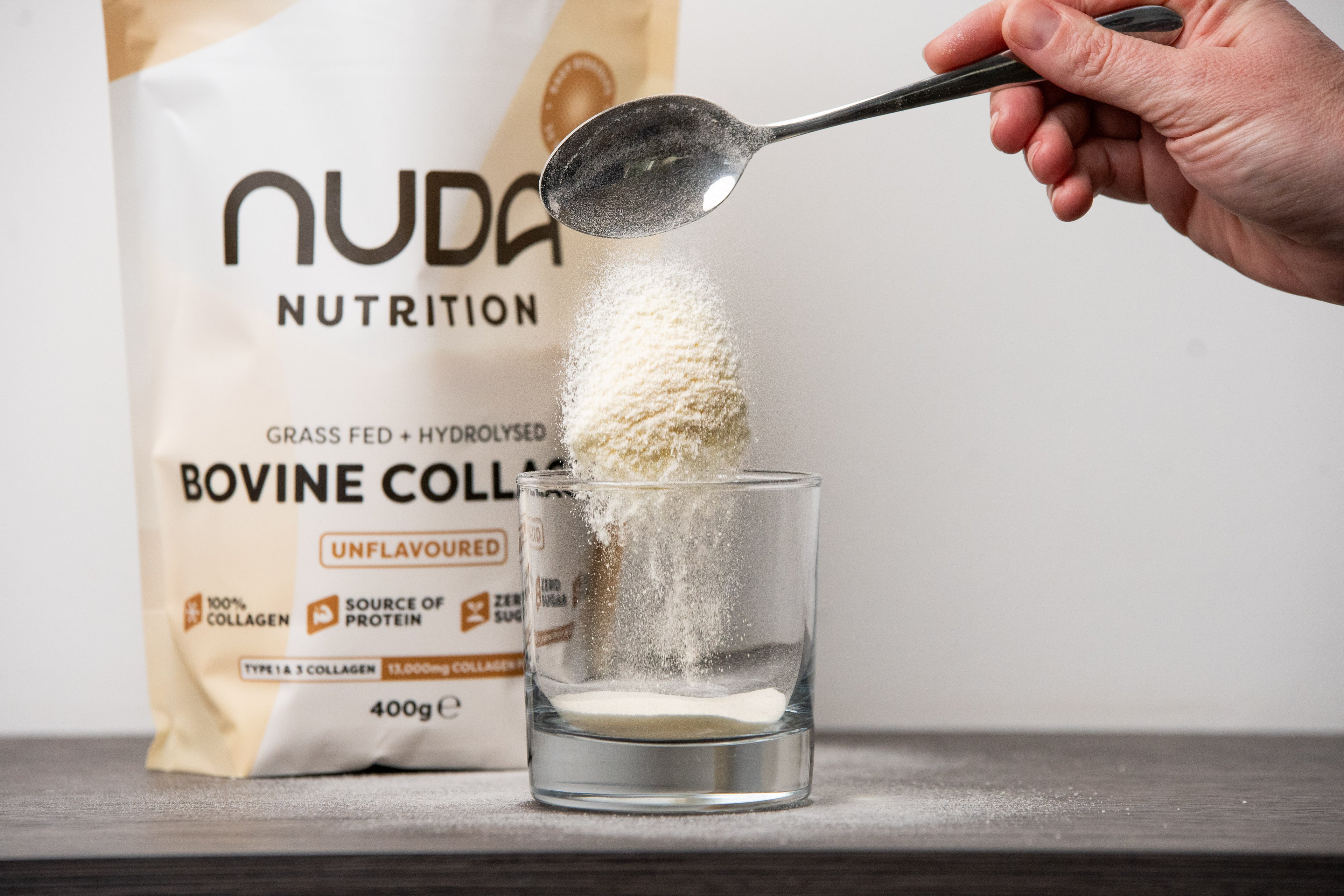 Nuda Nutrition bovine collagen powder being poured into a glass with a spoon.